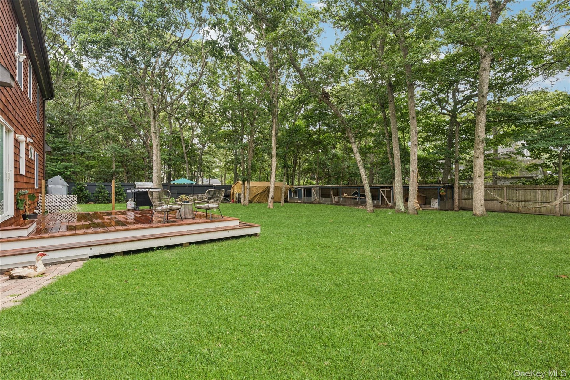 Expansive green lawn with mature trees, a multi-level wood-finish deck, and wood siding on the exterior