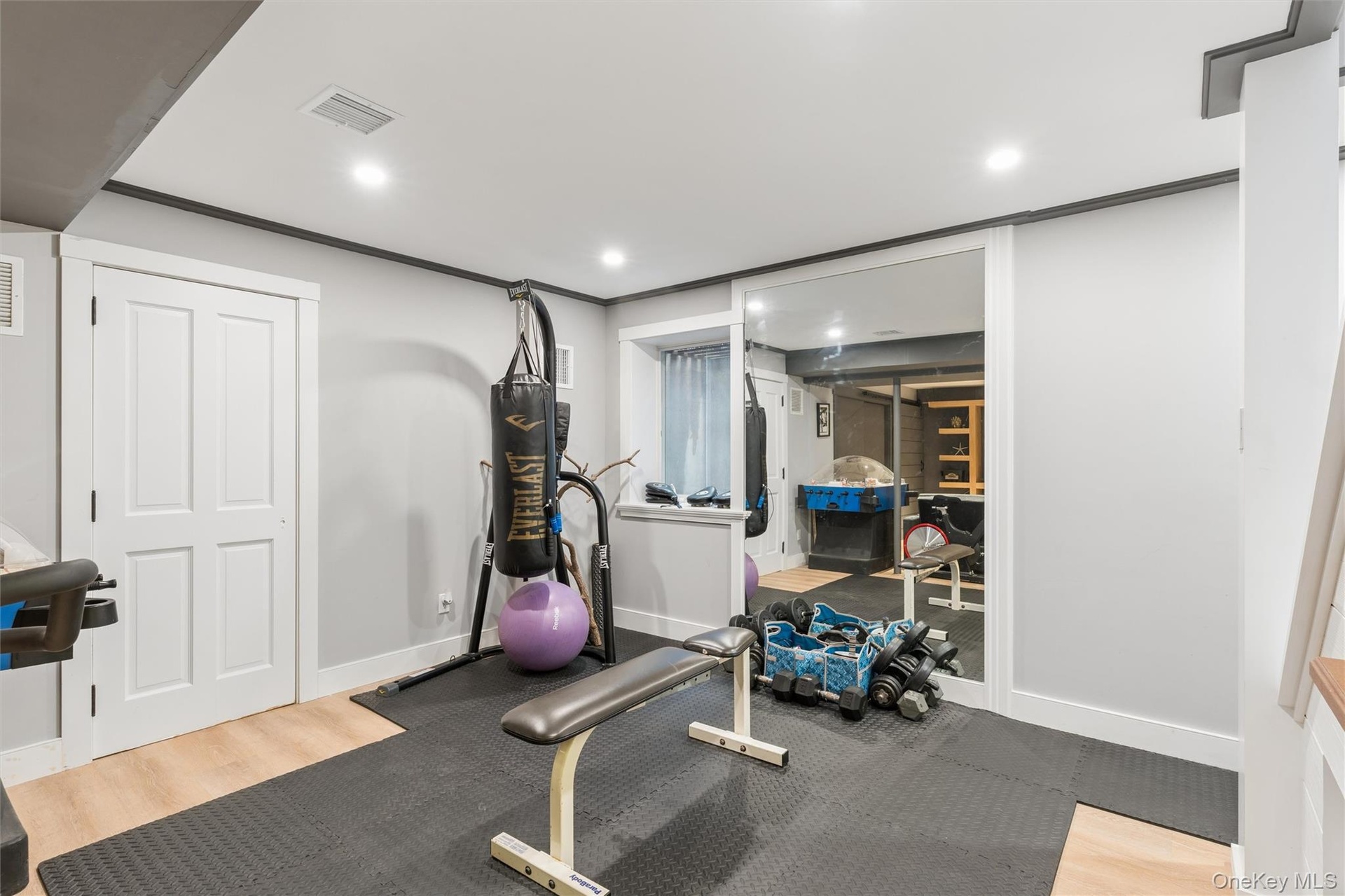 Recessed lighting, wood-finish flooring, white paneled door, mirrored wall, and a staircase with wood treads