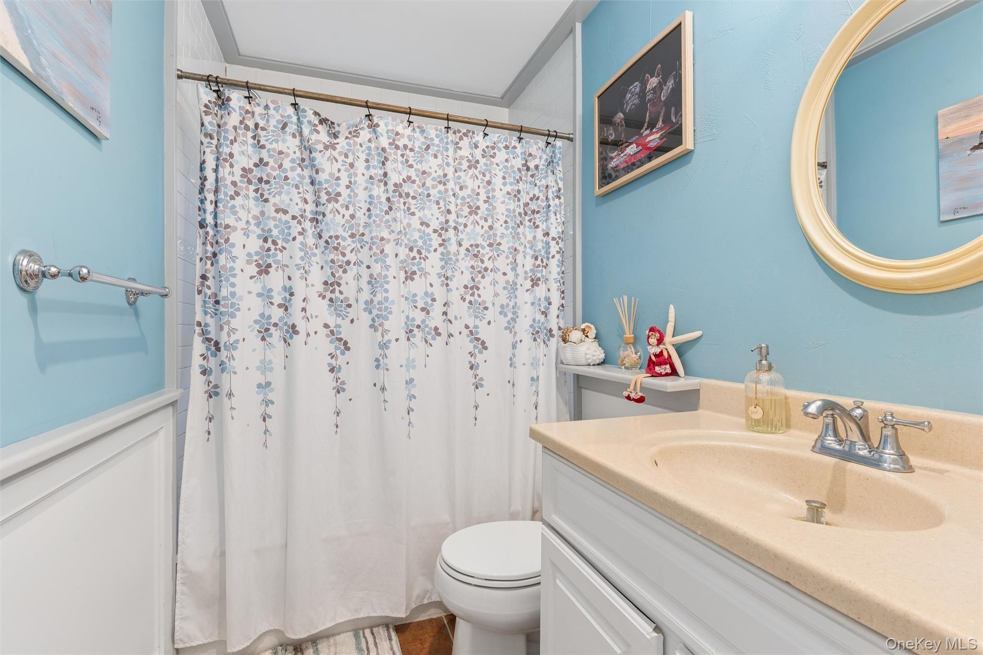 White paneled wainscoting with a light blue wall, a built-in vanity with a single basin, and a wall-mounted oval mirror
