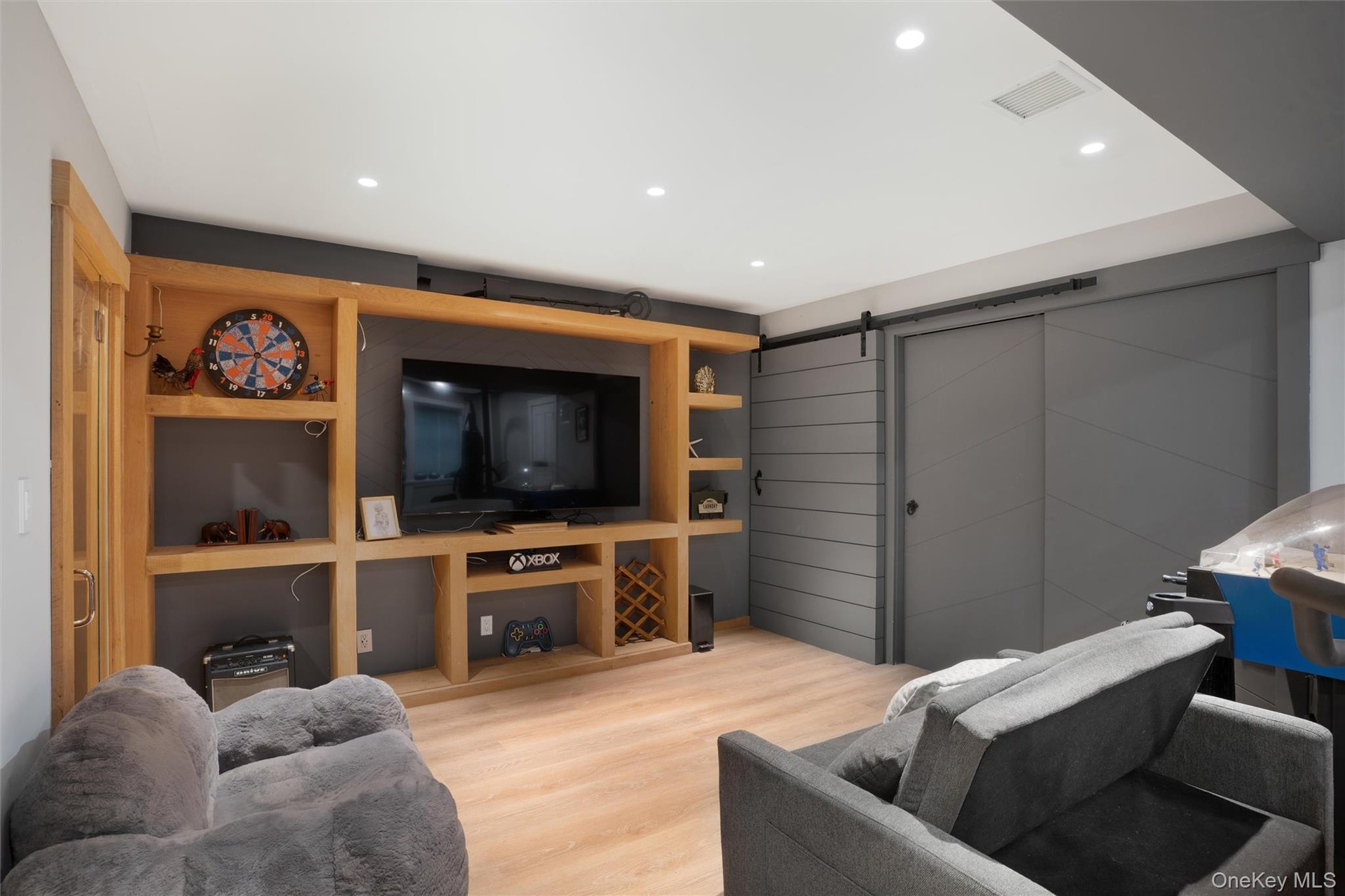 Recessed lighting, wood-finish flooring, built-in media console with shelving, and sliding barn doors with matte black hardware