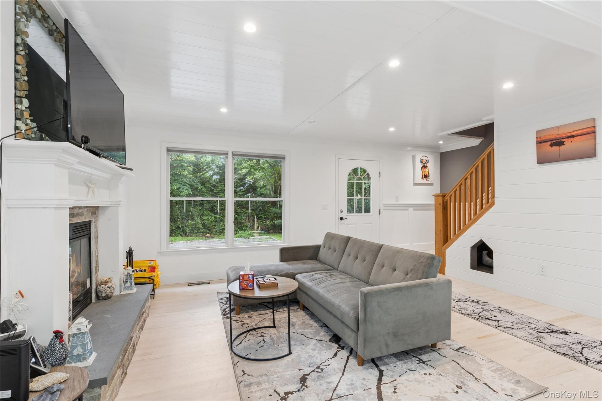 Recessed lighting, wood-finish flooring, a white-painted fireplace with a stone hearth, a multi-pane entry door, and a natural wood staircase with a b