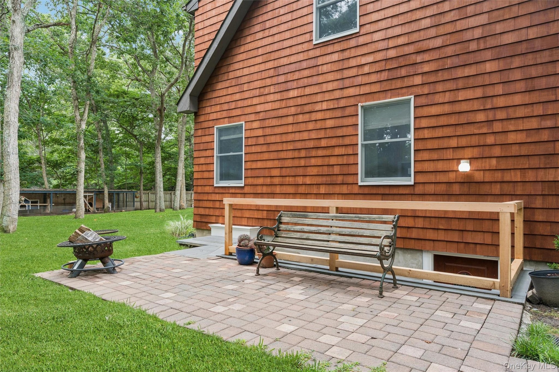 Cedar shake siding, paver patio, established lawn, mature trees, and a wooden railing