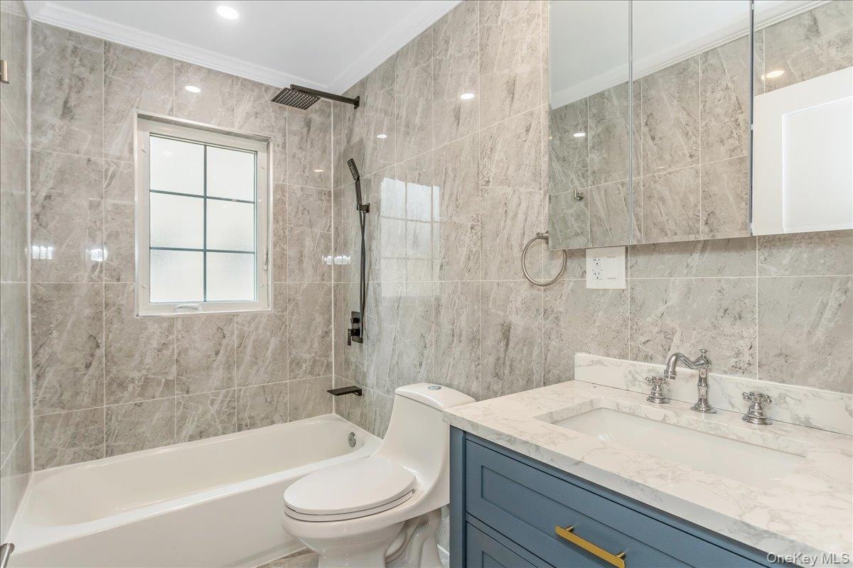 Bathroom with bathing tub / shower combination, tile walls, vanity, and ornamental molding