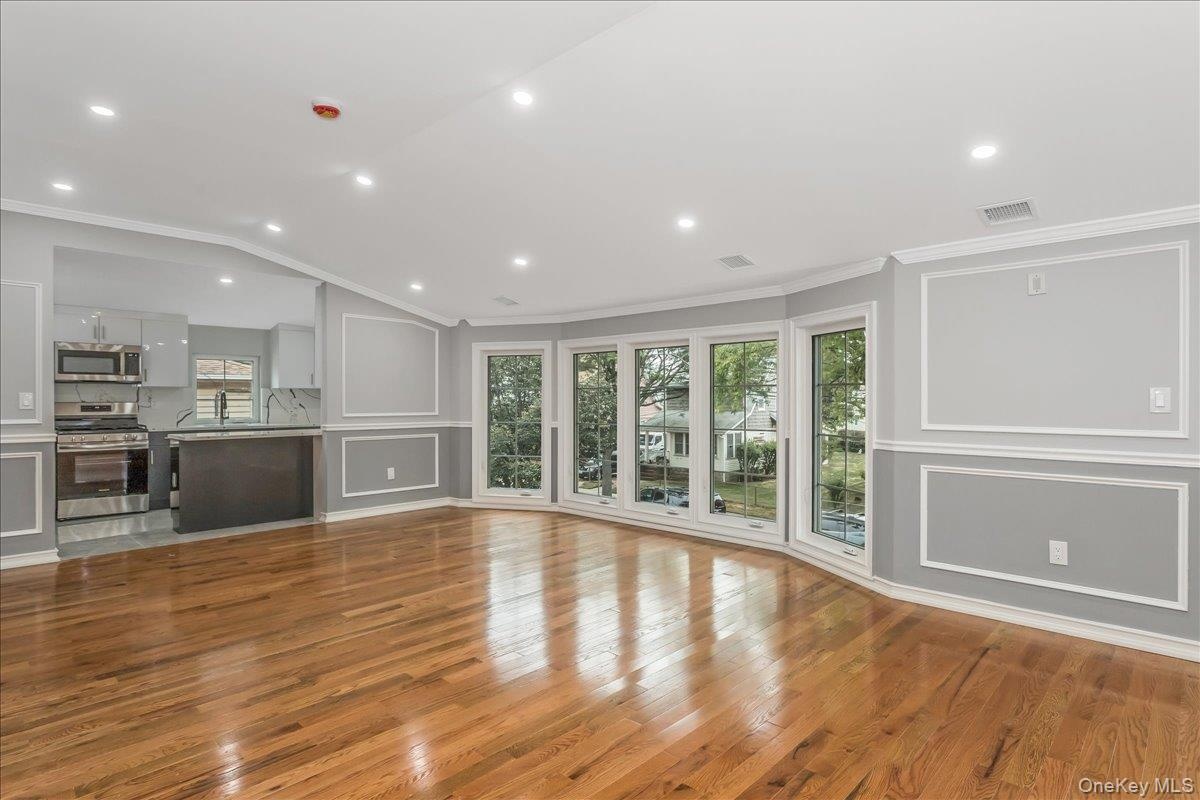 Unfurnished living room featuring plenty of natural light, light wood finished floors, a decorative wall, ornamental molding, and vaulted ceiling