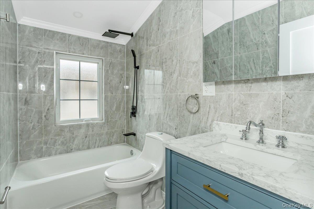 Bathroom featuring tile walls, shower / bath combination, vanity, and ornamental molding
