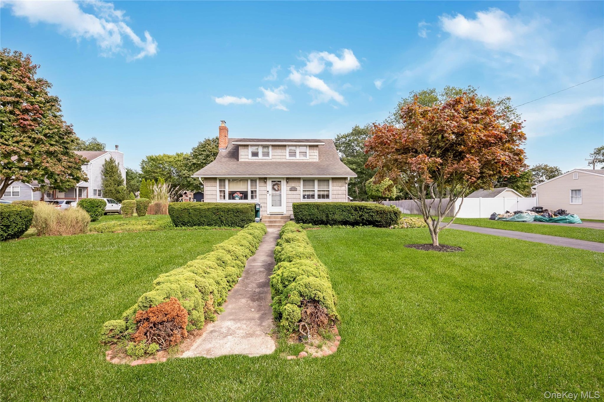 Traditional-style residence with dormer windows, a prominent brick chimney, and a concrete pathway bordered by hedges