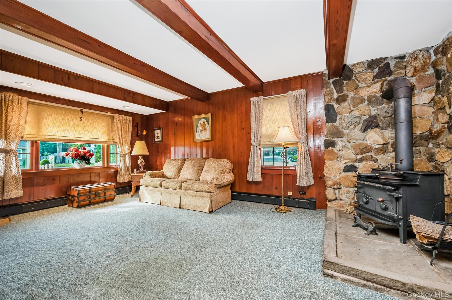 Wood paneling, exposed ceiling beams, stone accent wall, and a built-in wood-burning stove with a stone hearth