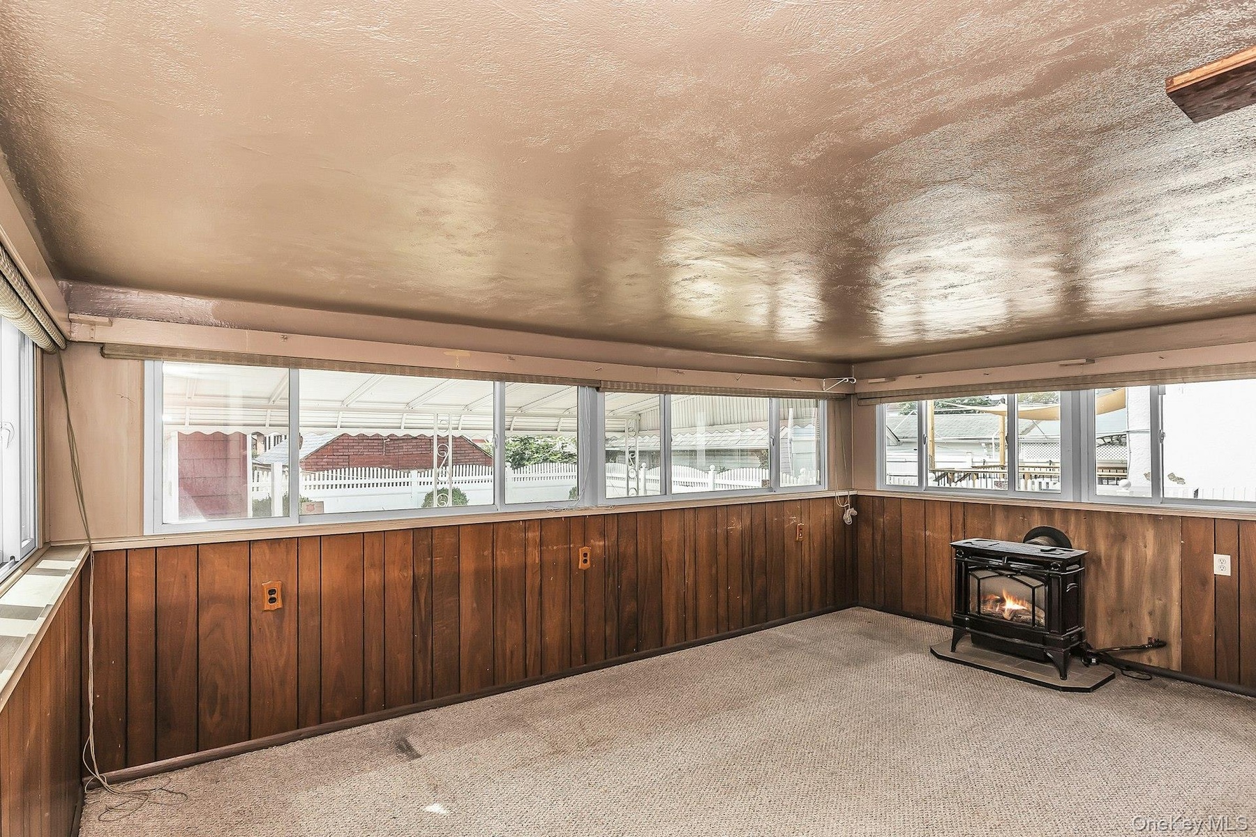 Sun Room featuring wood paneling, multiple windows, and a black cast iron stove