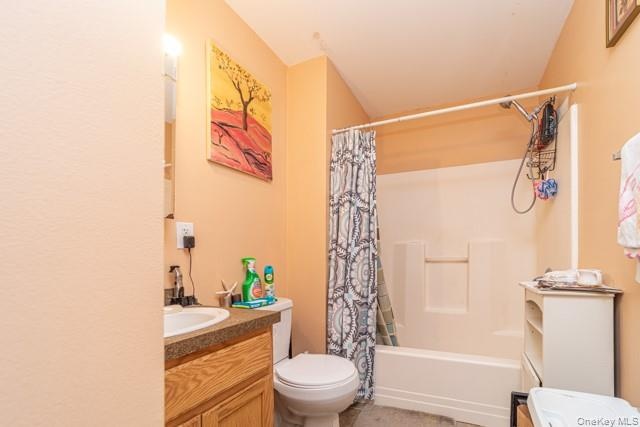 Bathroom featuring a wood-finish vanity with an integrated sink, a commode, and a shower-tub combination
