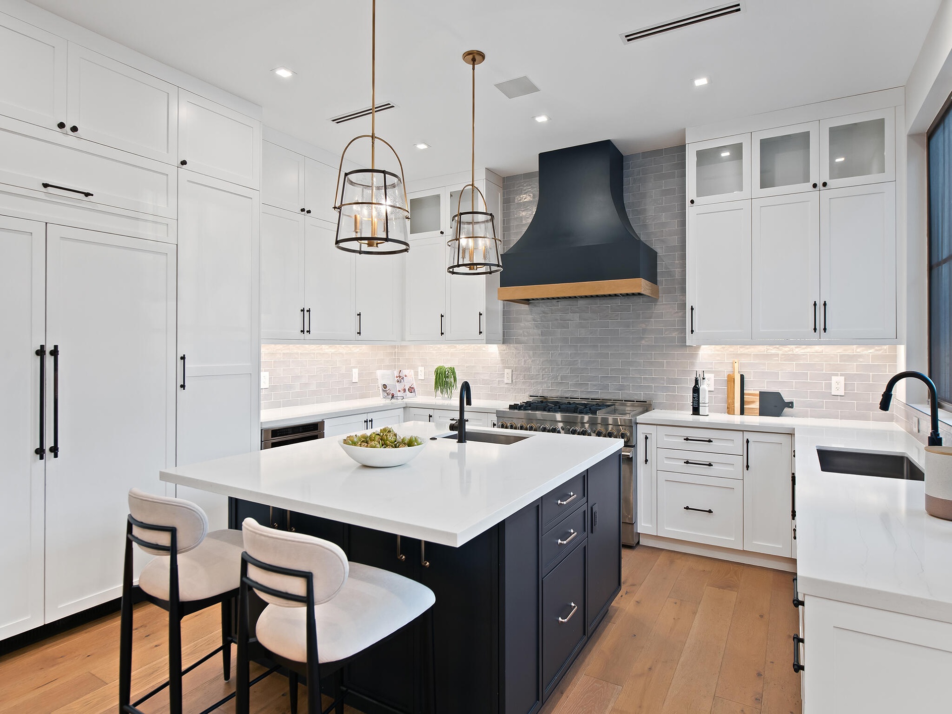 Kitchen with white cabinetry, charcoal island and gold pendants