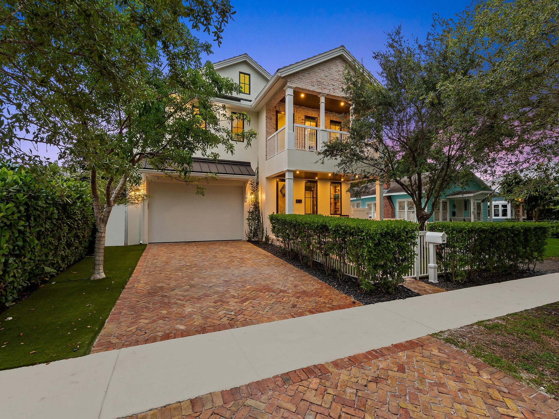 Front exterior at dusk with brick driveway and mature trees