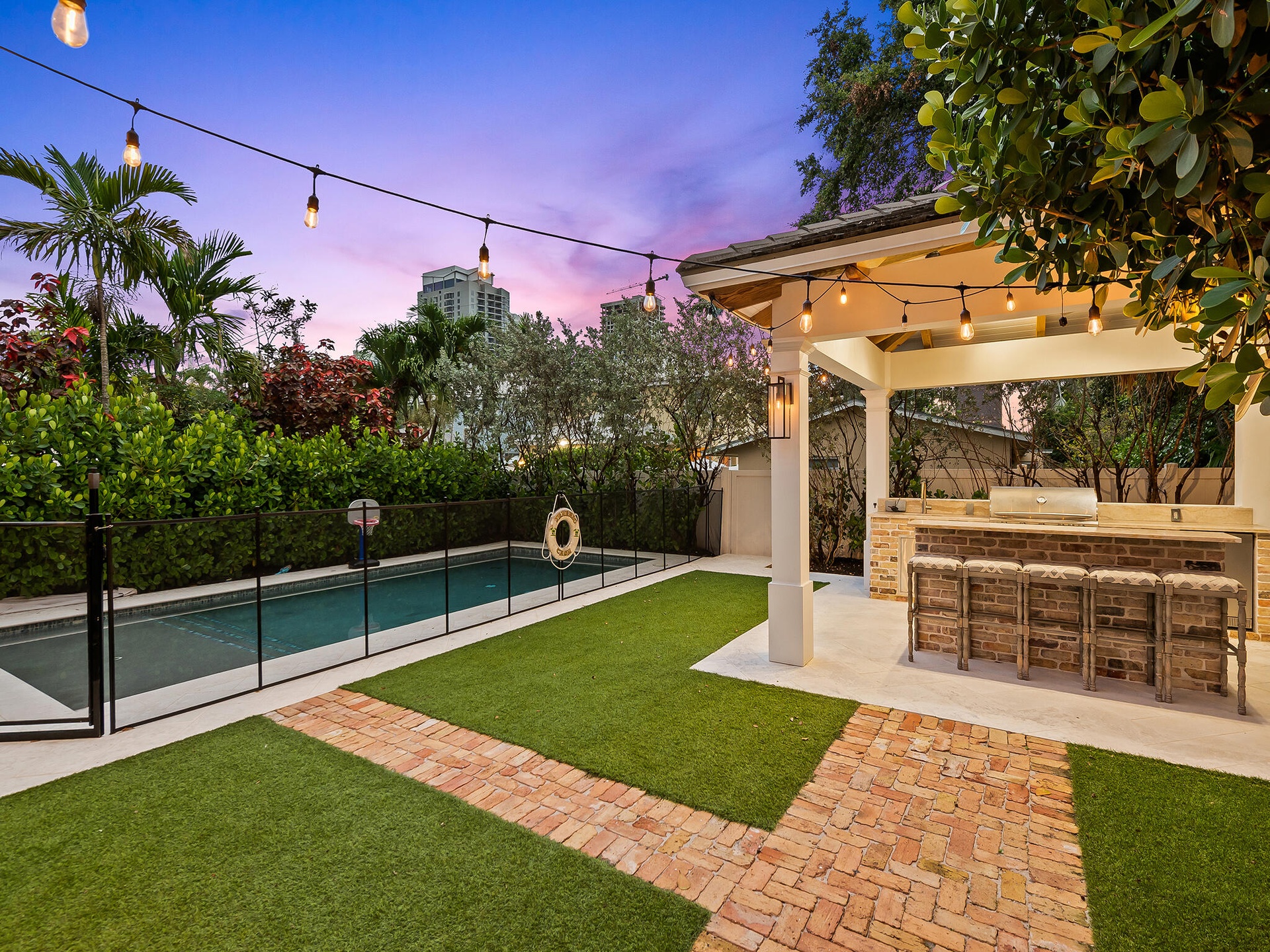 Backyard at dusk with pool, turf and lit pergola