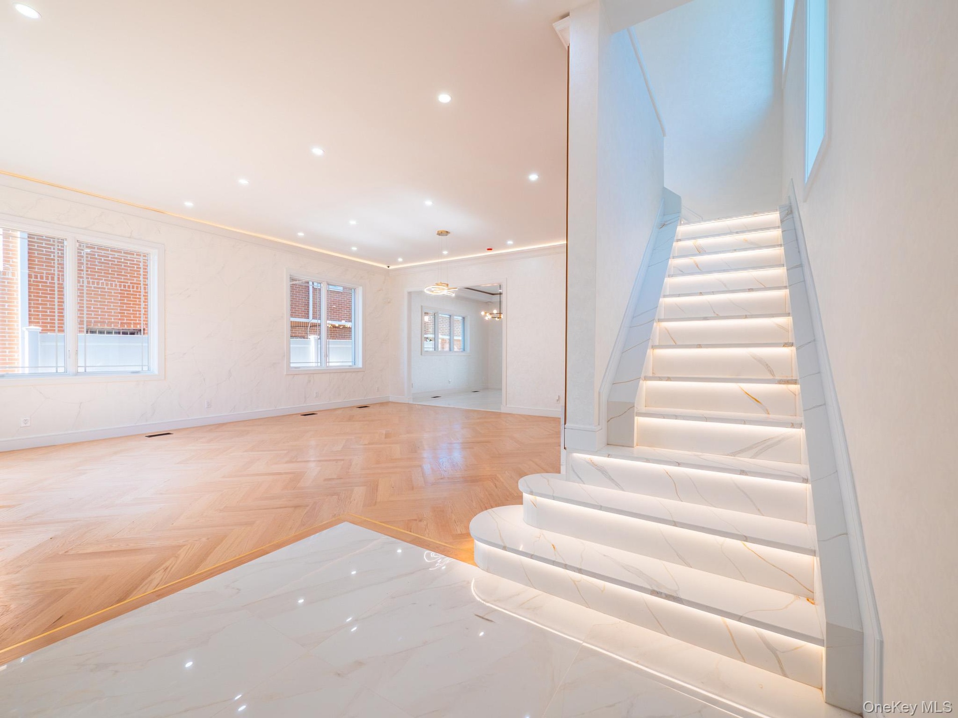 Herringbone wood-finish flooring, recessed ceiling lighting, cove lighting, marble-look tile entry, and illuminated staircase