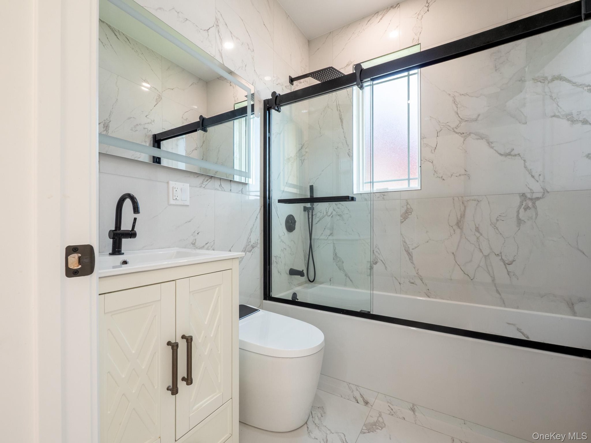 Full-height marbled tile, sleek black-framed shower enclosure, white vanity with textured cabinet doors, contemporary black faucet, and modern toilet