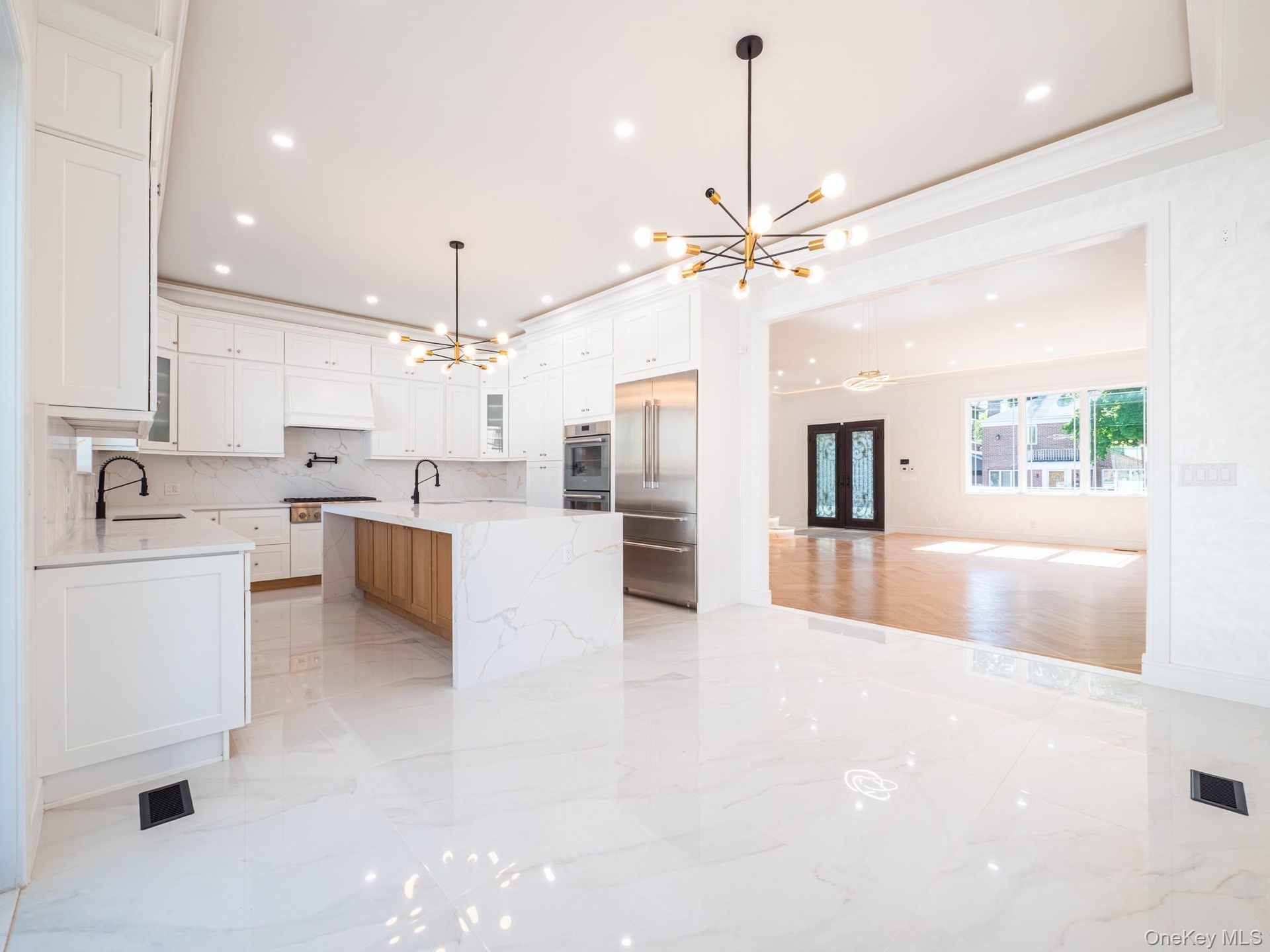 Gourmet kitchen featuring white shaker cabinetry, polished tile flooring, a large island with waterfall countertops, and integrated stainless steel ap