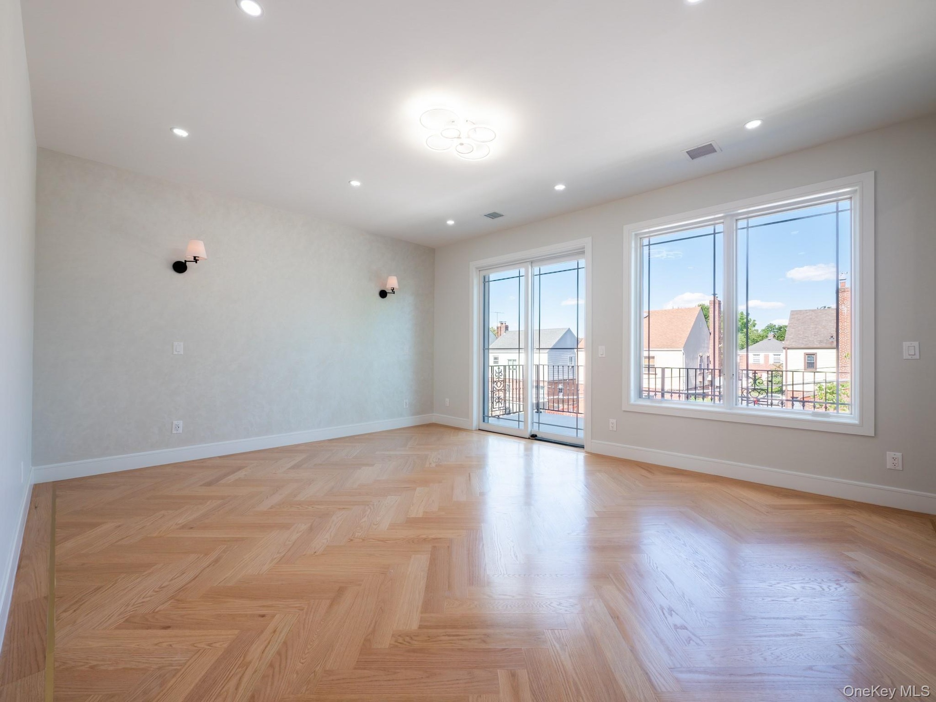 Herringbone wood-finish flooring, recessed lighting, and wall-mounted sconces