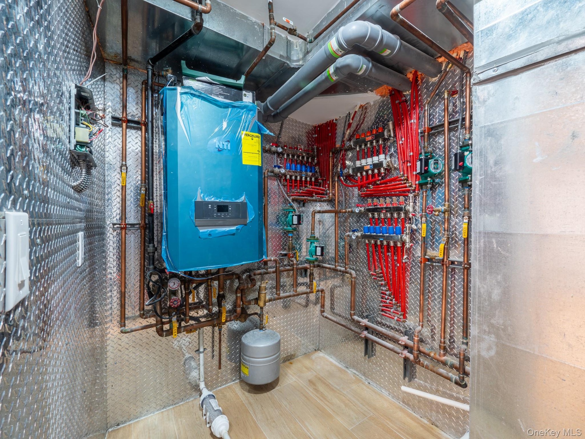 Utility room with diamond plate wall paneling, extensive copper piping, and a large blue boiler system