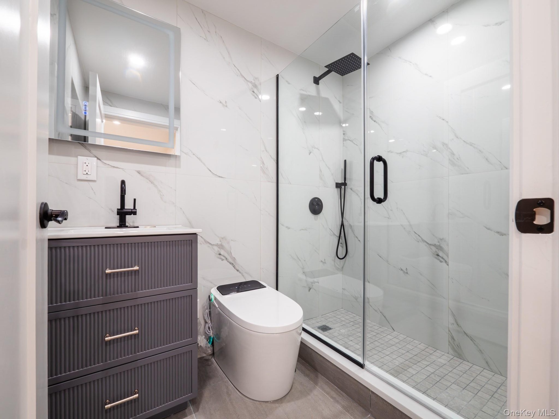 Modern bathroom featuring a glass-enclosed shower with matte black fixtures, a white tiled shower base, and a vanity with a white countertop