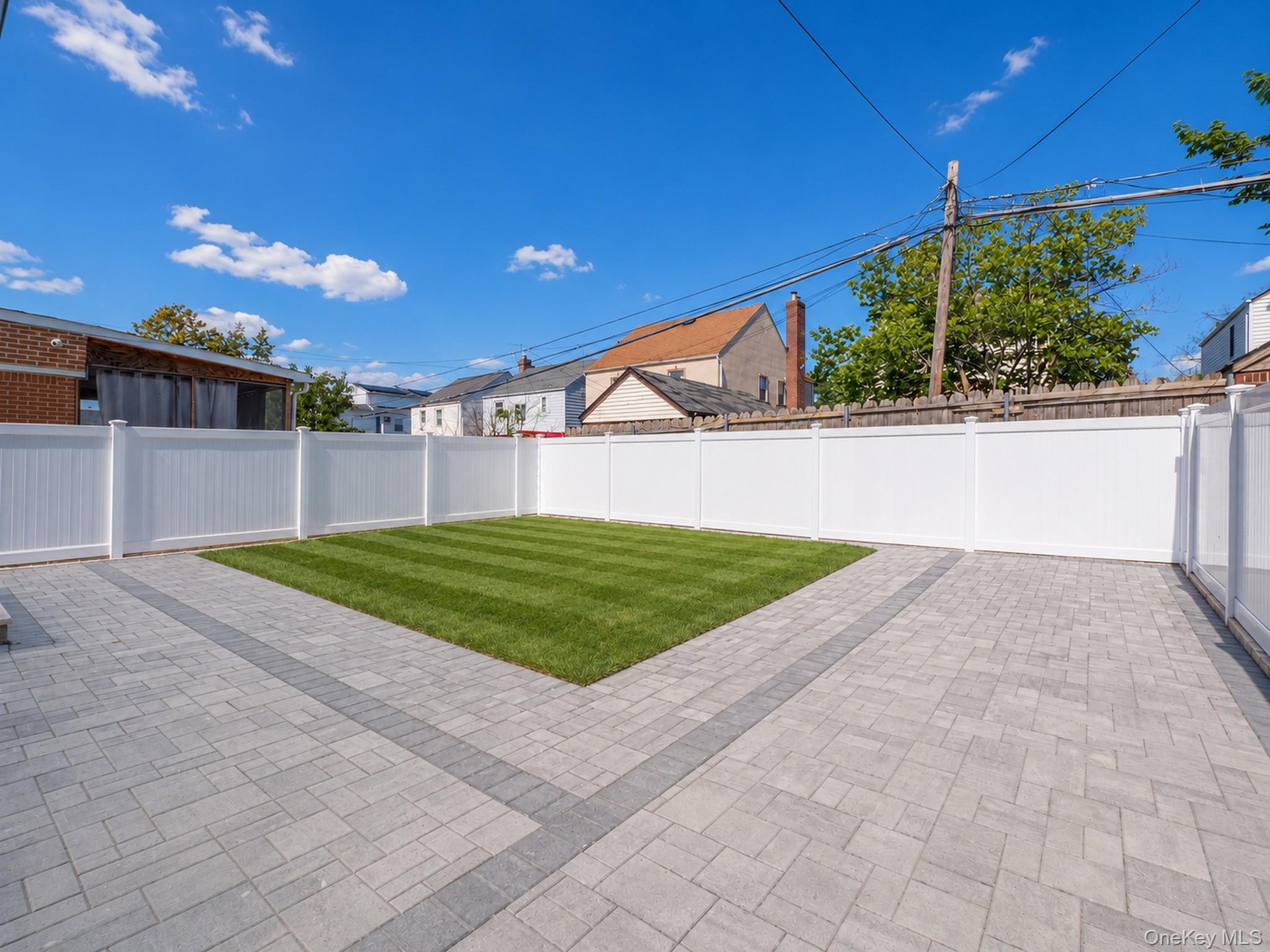 Expansive backyard featuring a manicured lawn, paver patio with a contrasting border, and white privacy fencing