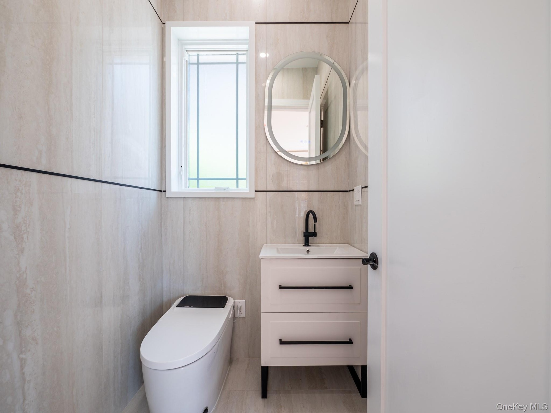 White floating vanity with a vessel sink, matte black faucet, and an illuminated oval mirror