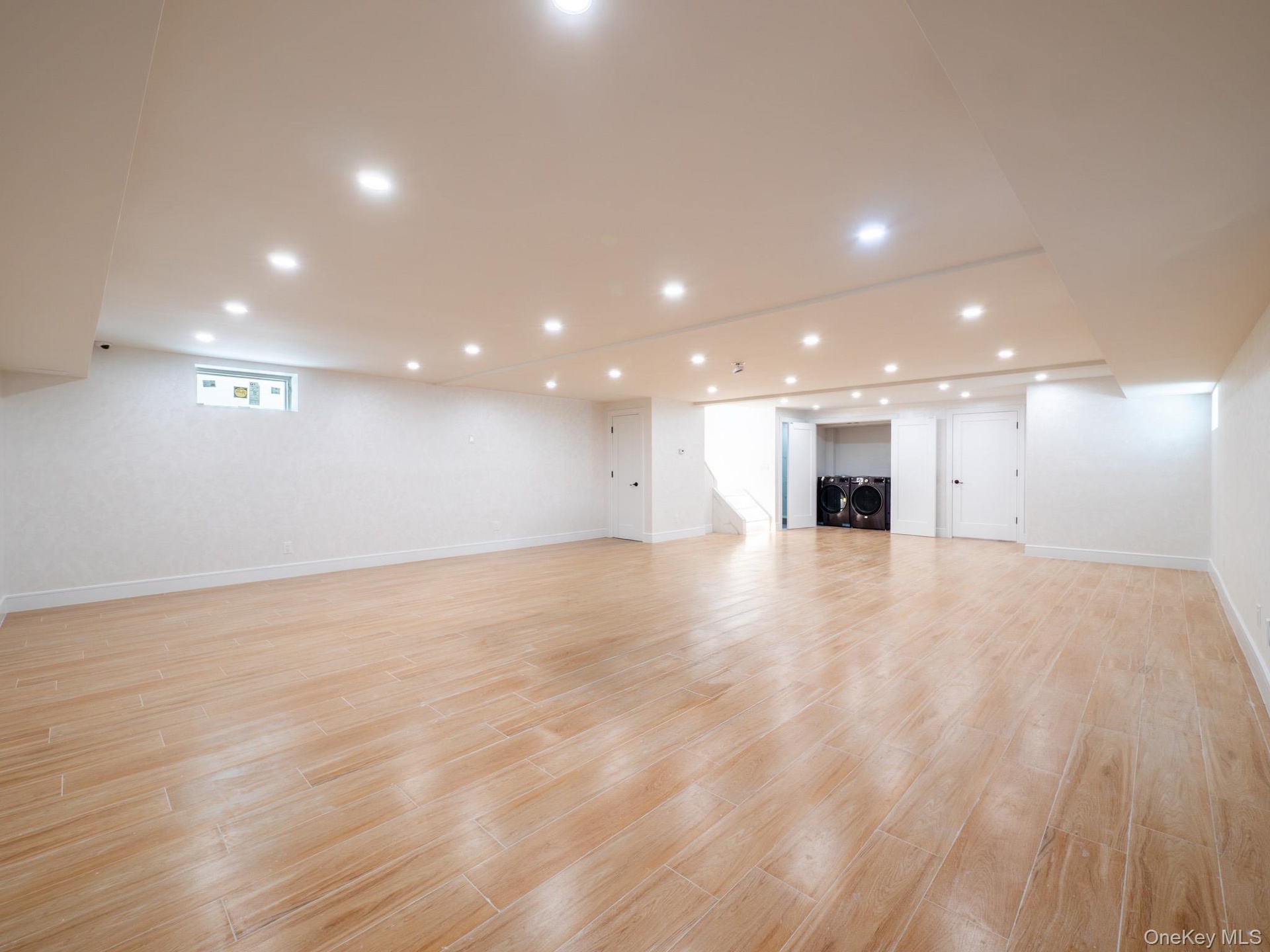 Expansive open-plan room with recessed lighting, wood-finish flooring, and white walls
