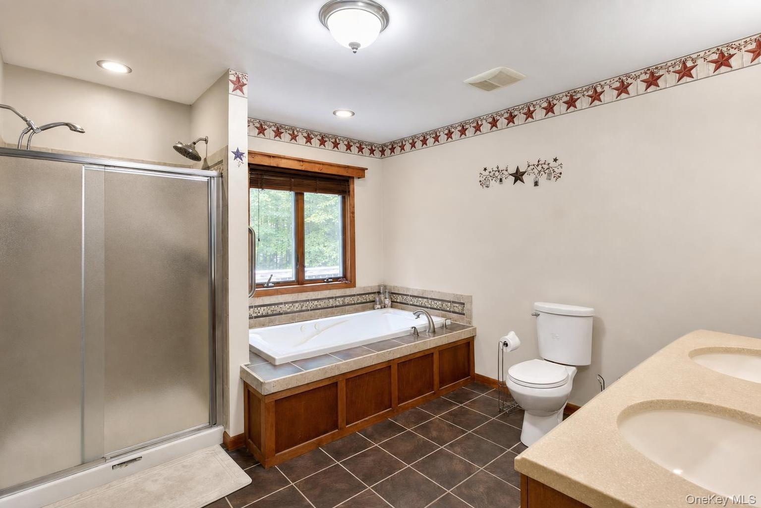 Dual vanity with integrated sinks, built-in Jacuzzi soaking tub, separate shower with frosted glass enclosure, and tiled flooring