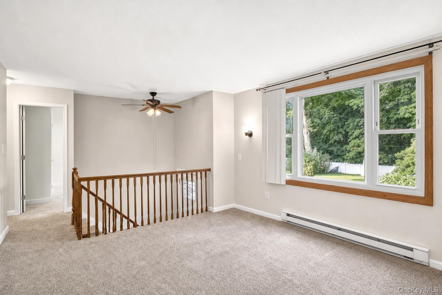 Carpeted interior with a large window, wooden railing, and a ceiling fan