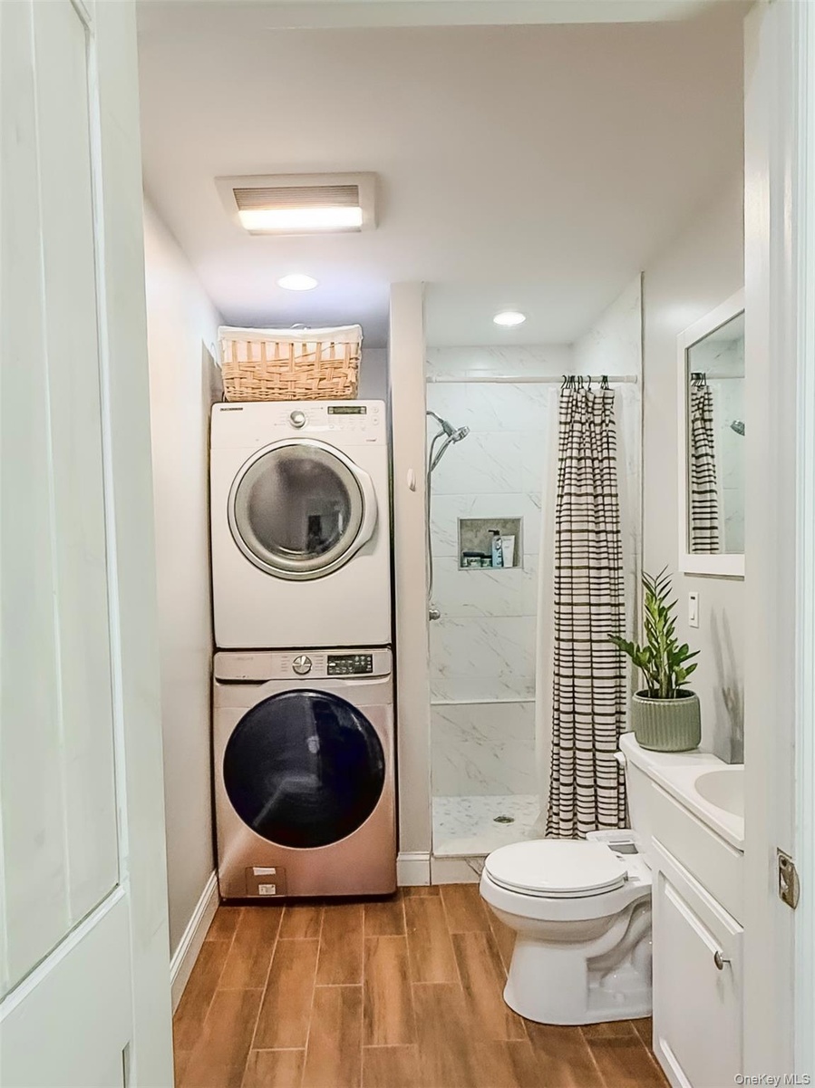 Cottage full bathroom with wood-finish flooring, stacked laundry appliances, walk-in shower with glass enclosure, recessed lighting, and a vanity with