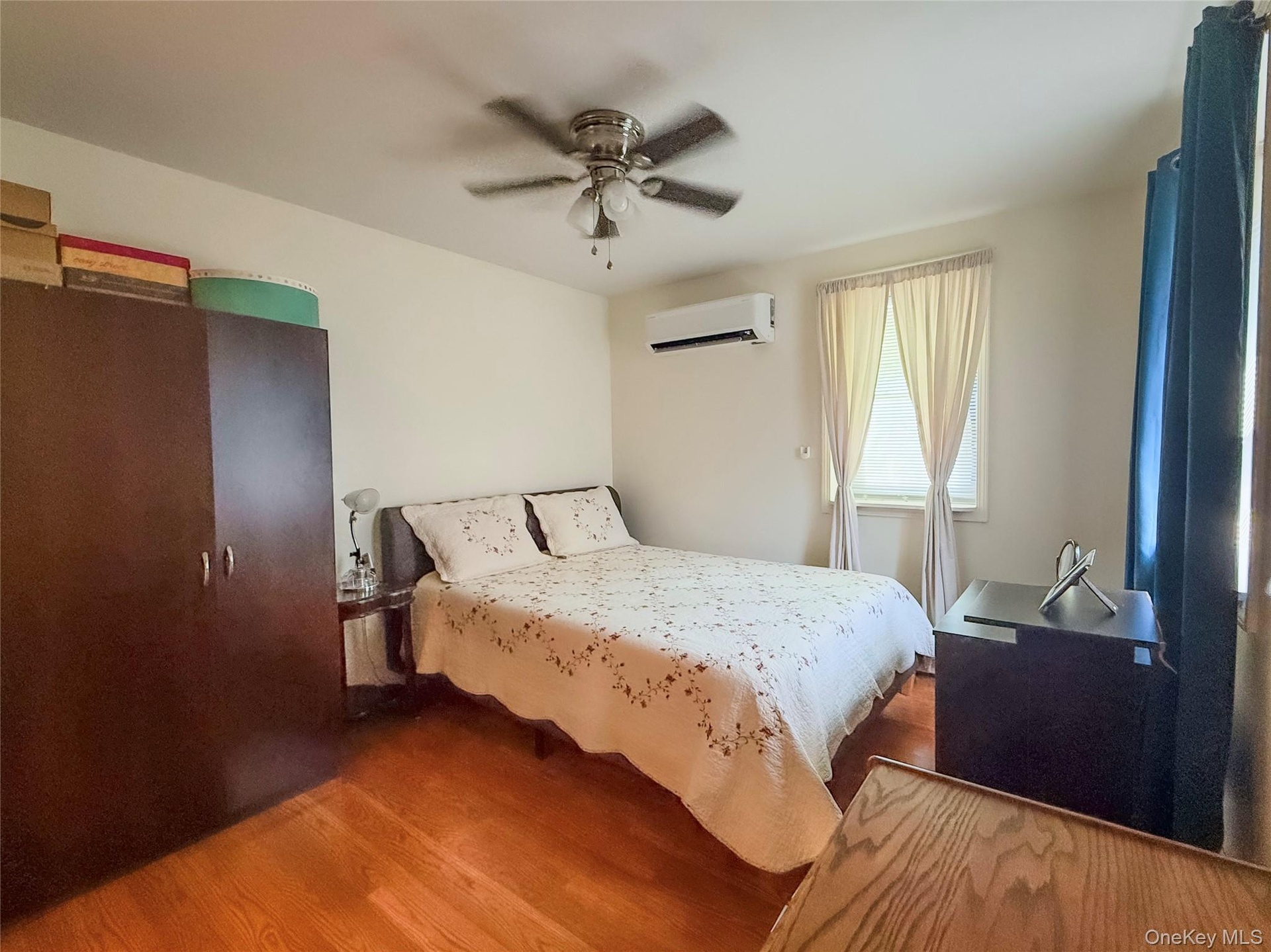 Lower apt bedroom Hardwood flooring, ceiling fan, and window with curtains