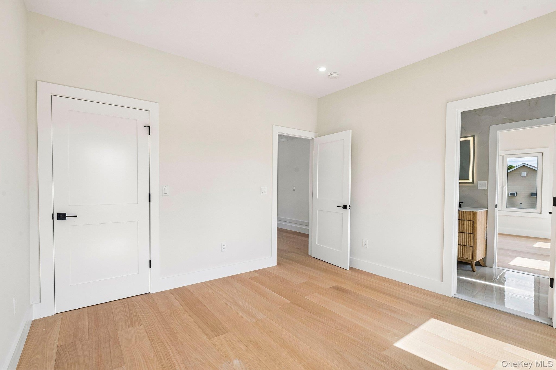 Light wood-finish flooring, recessed ceiling lighting, two-panel interior doors with black hardware, white baseboards