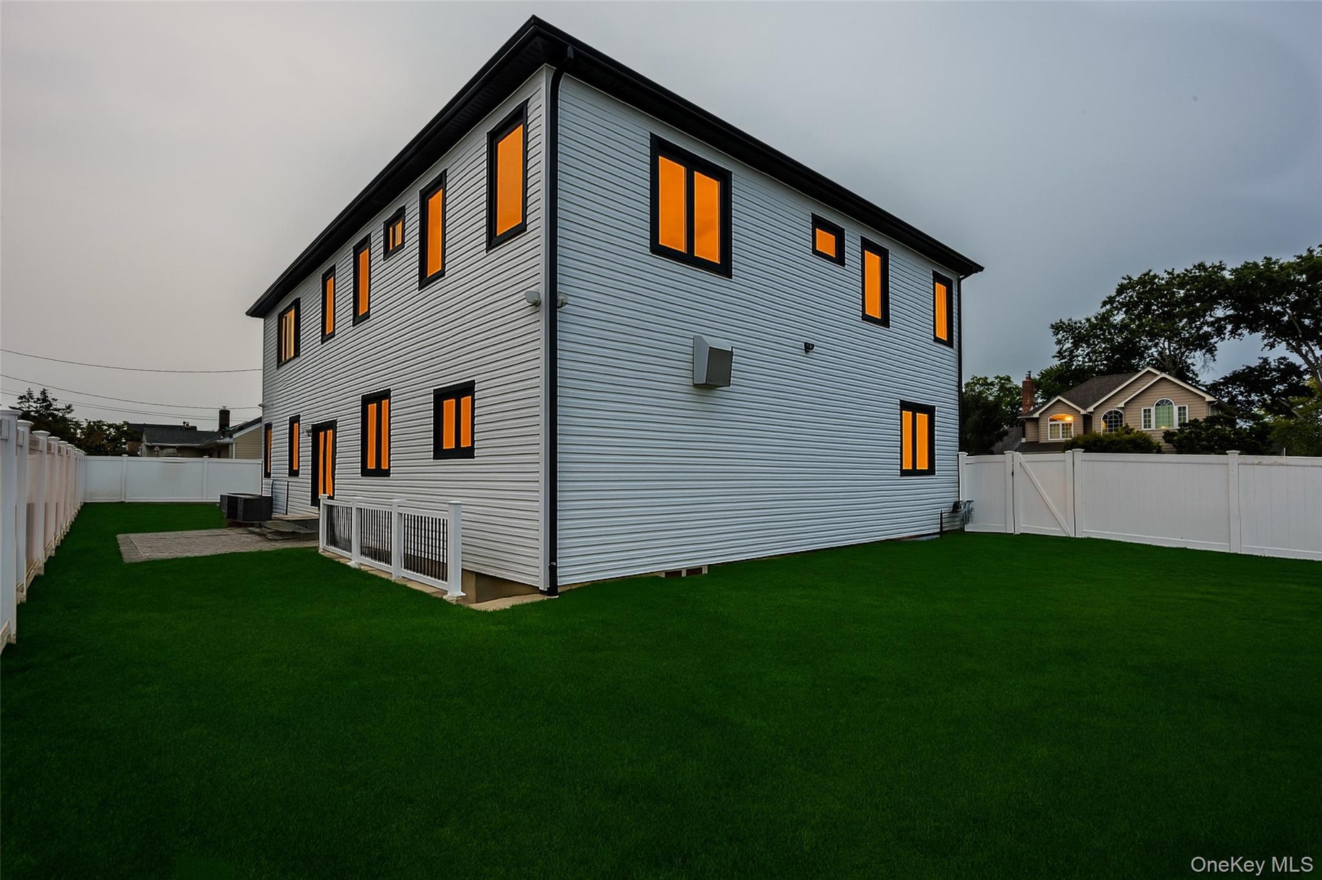 Fenced yard with artificial turf, a paver patio, and a two-story exterior featuring white siding and black trim windows