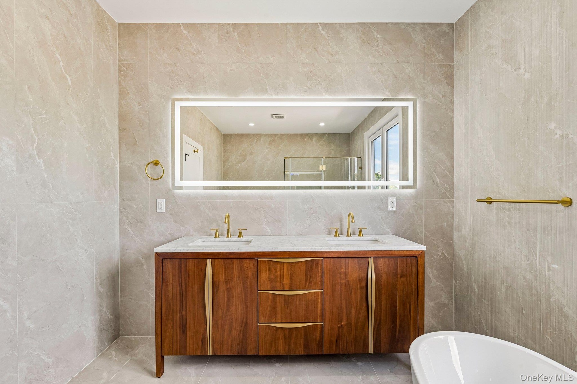 Dual sink vanity with wood-finish cabinetry, integrated countertop, and brass-finish fixtures