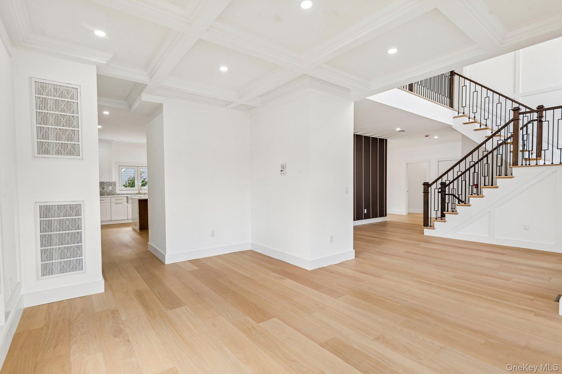 Light wood-finish flooring, coffered ceiling with recessed lighting, and a staircase featuring dark wood handrails with decorative metal balusters