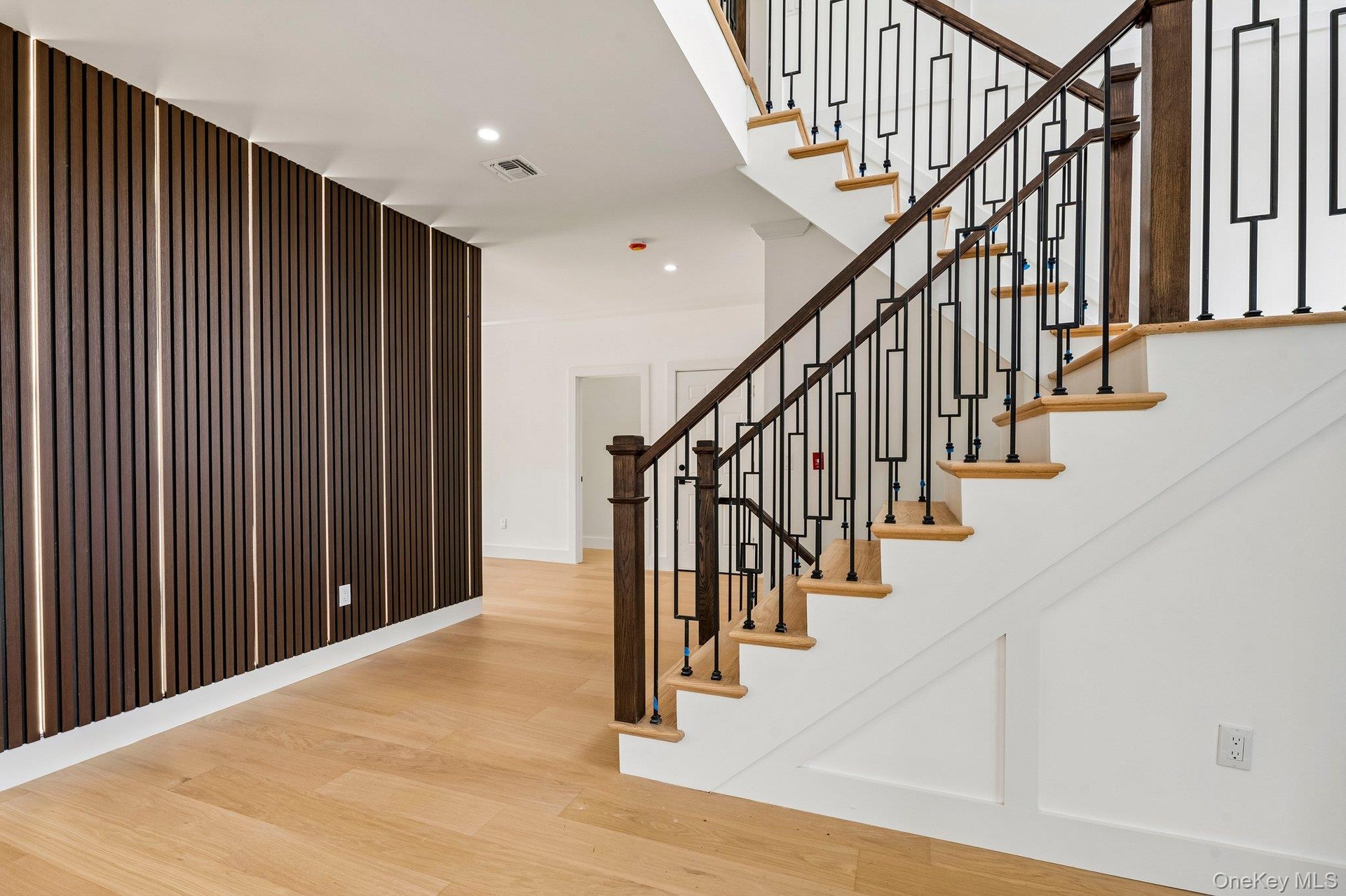 Hardwood flooring, custom wall paneling with integrated lighting, recessed ceiling lighting, staircase with decorative metal balusters, and a rich woo