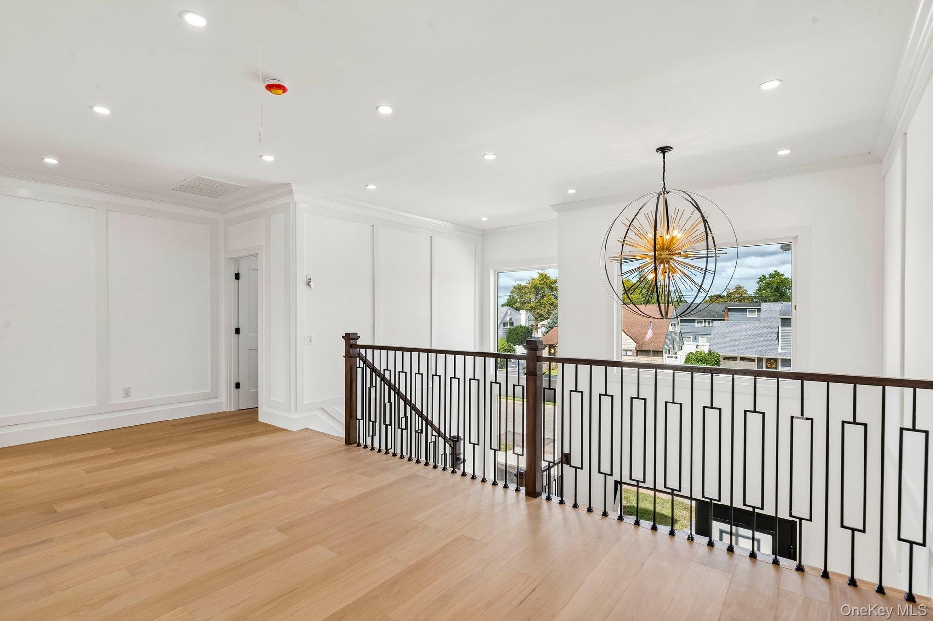 Hardwood flooring, contemporary chandelier, recessed lighting, white paneled walls, and dark metal stair railing with wood newel posts