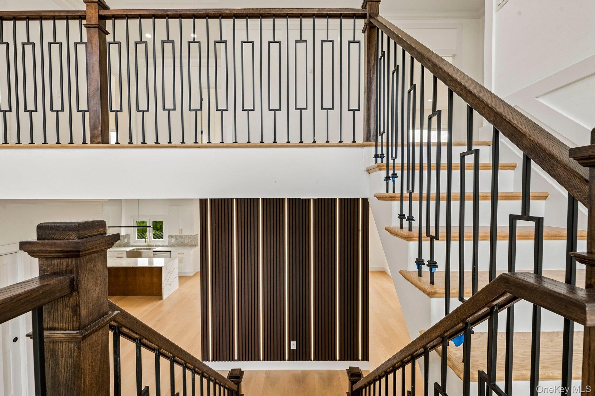 Wood-finish staircase with black metal balusters, hardwood flooring, and a decorative slatted wall panel