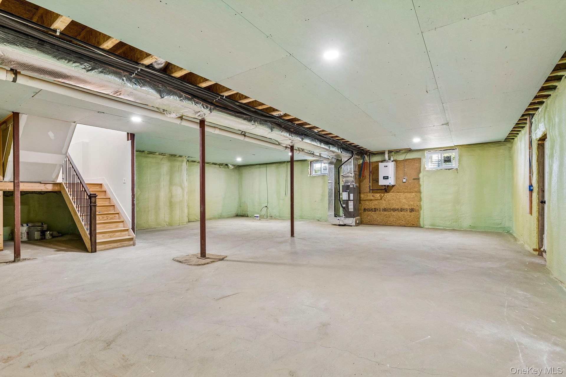 Spacious unfinished lower level with concrete flooring, recessed lighting, exposed ceiling joists, and a finished wooden staircase with railing
