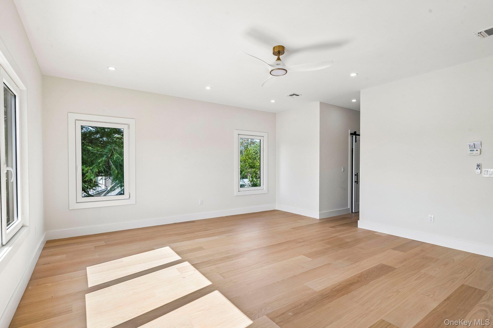 Light wood-finish flooring, recessed lighting, white walls, multiple windows, and a modern ceiling fan