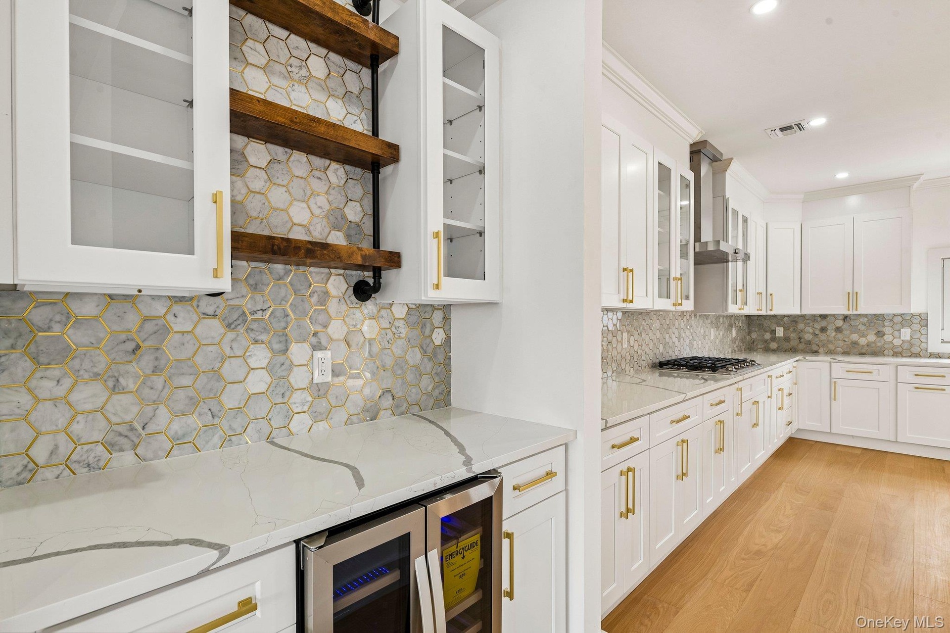White cabinetry with gold-tone hardware, hexagon tile backsplash, quartz countertops, built-in beverage refrigerator, and wood-finish flooring