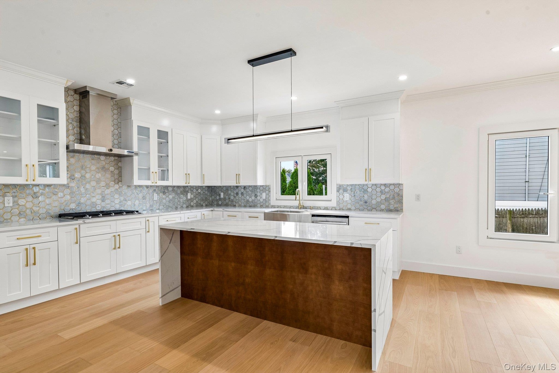 White shaker cabinetry with gold-tone hardware, hexagonal tile backsplash, stainless steel range hood, integrated kitchen island with contrasting wood