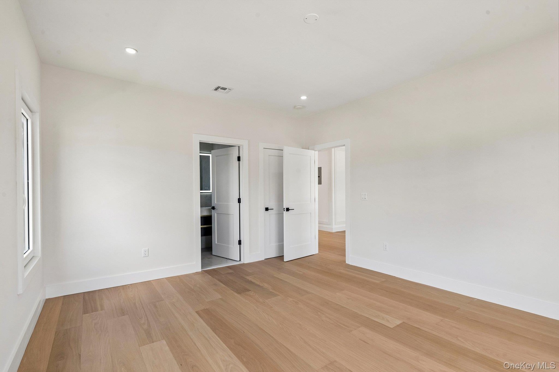 Recessed lighting, wood-finish flooring, white walls, white trim, and white doors with matte black hardware