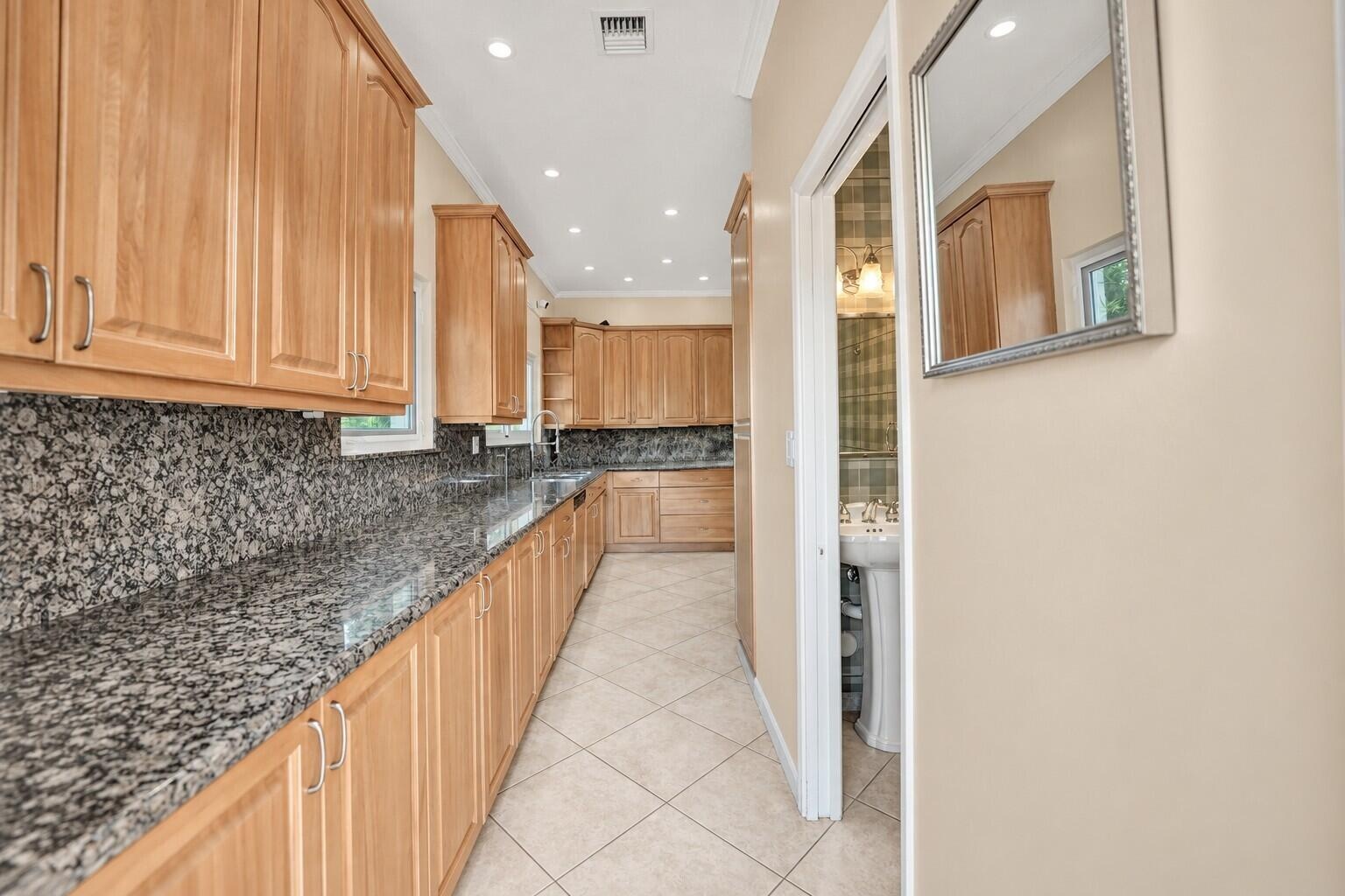 Extensive granite countertops with matching backsplash, light wood cabinetry, recessed lighting, and tile flooring. Wall color has been virtually enha