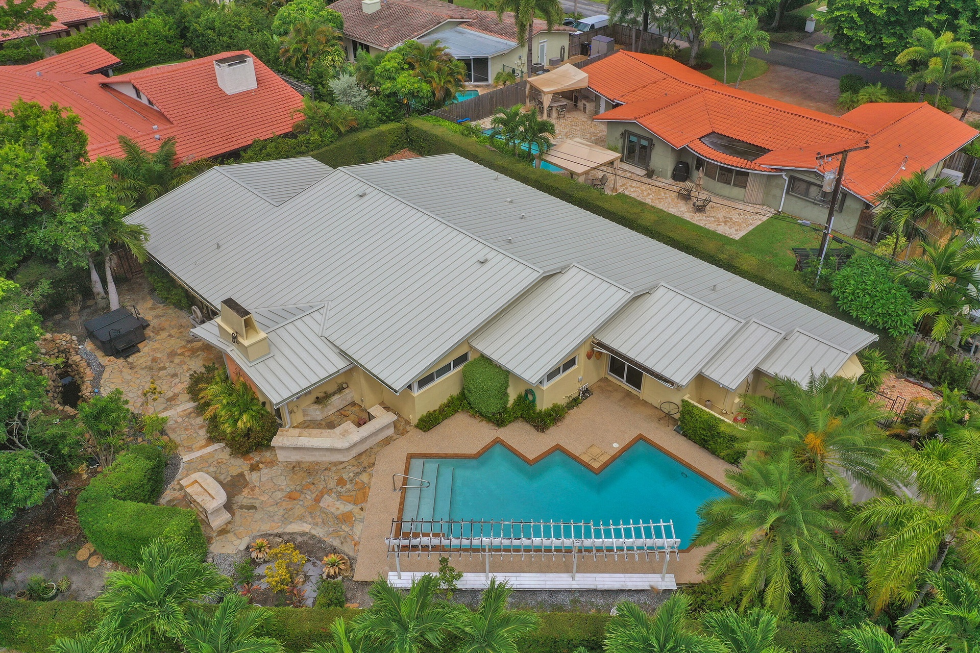 Expansive residence featuring a multi-gabled roofline, a geometric-shaped swimming pool, and extensive stone hardscaping