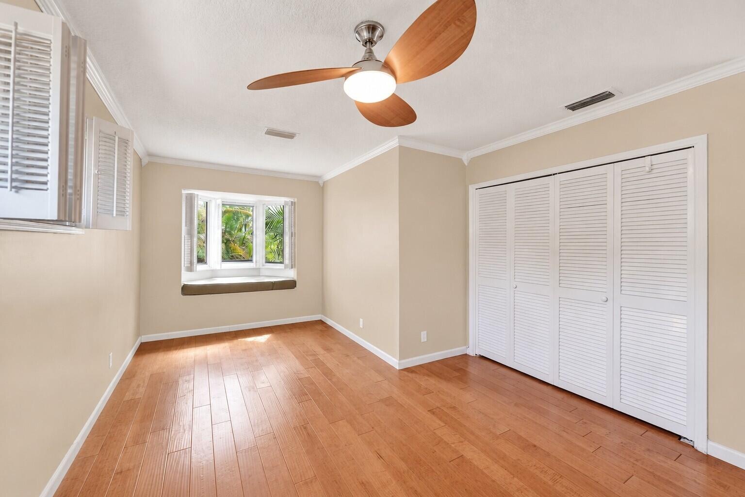 Hardwood flooring, bay window with integrated seating, white louvered bifold closet doors, crown molding, and ceiling fan with integrated lighting