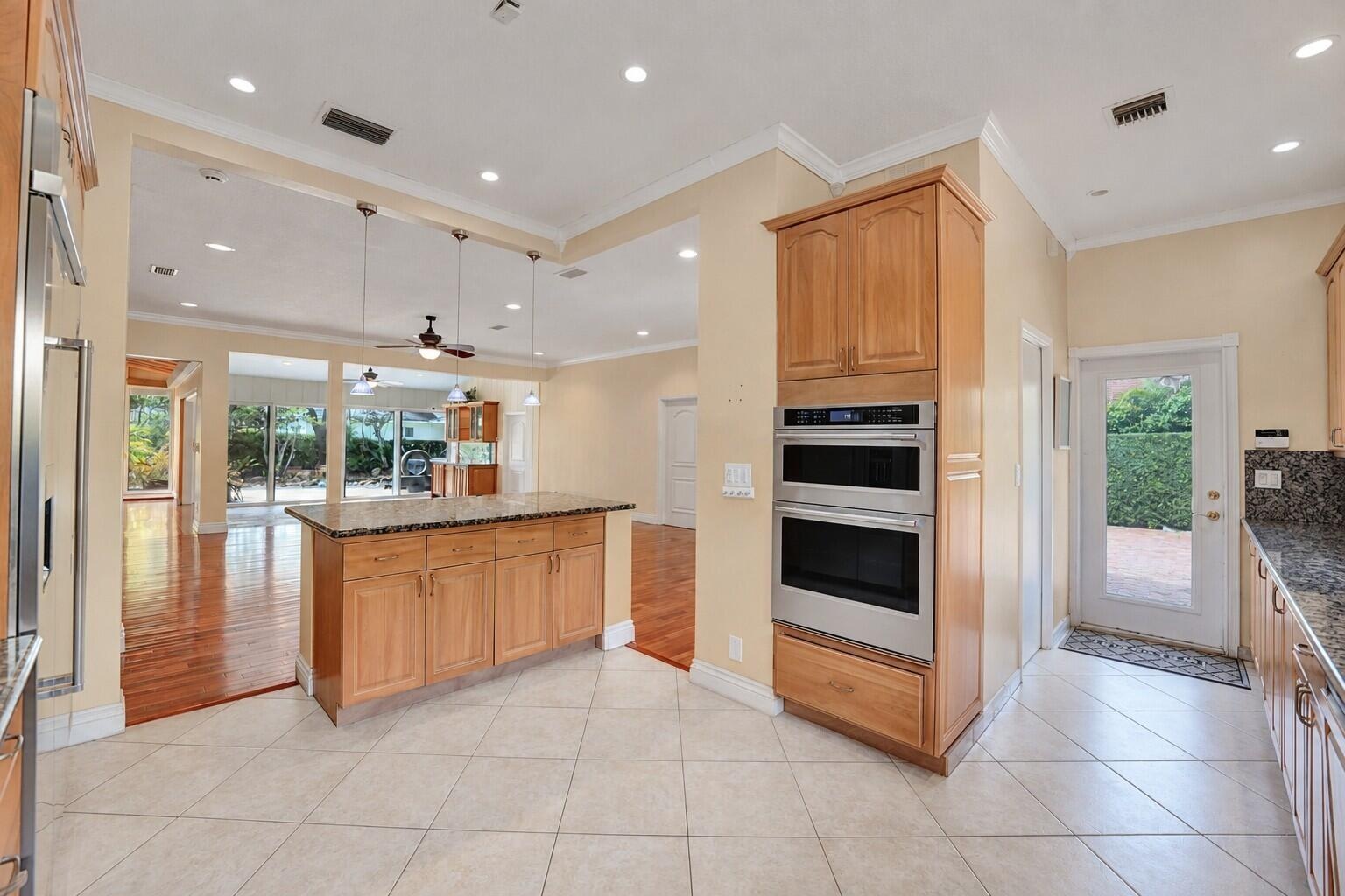 Kitchen featuring an island with granite countertops, built-in double ovens, light wood cabinetry, and recessed lighting. Wall color has been virtuall