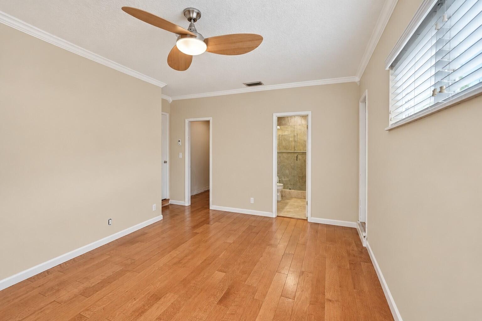 Wood-finish flooring with neutral wall tones, crown molding, and a ceiling fan with integrated lighting