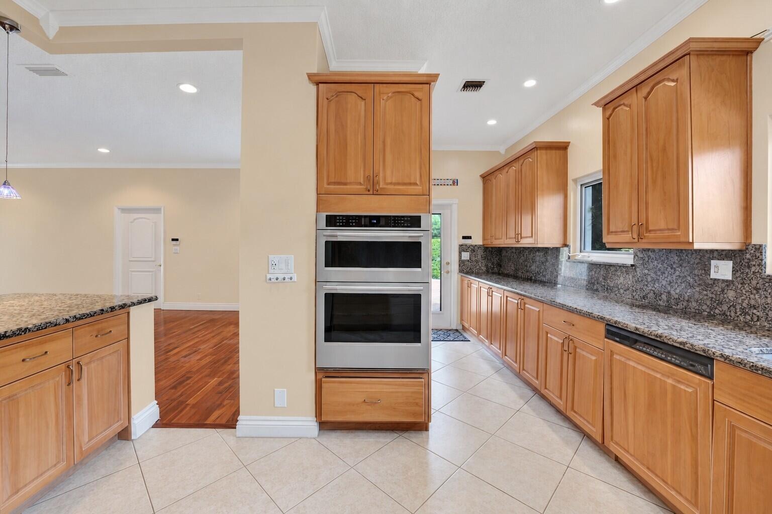 Kitchen featuring wood cabinetry, stainless steel double wall oven, neutral tile flooring, and dark speckled countertops. Wall color has been virtuall
