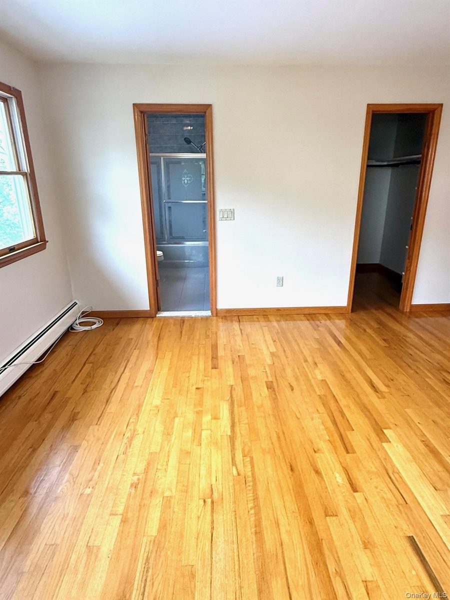 Primary bedroom/Primary bath and walk-in closet, baseboard heating unit, light wood-style floors, and a spacious closet
