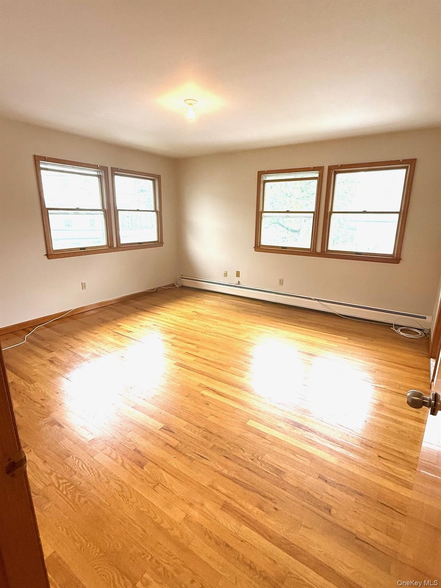 Primary bedroom featuring healthy amount of natural light, a baseboard heating unit, and light wood-style flooring
