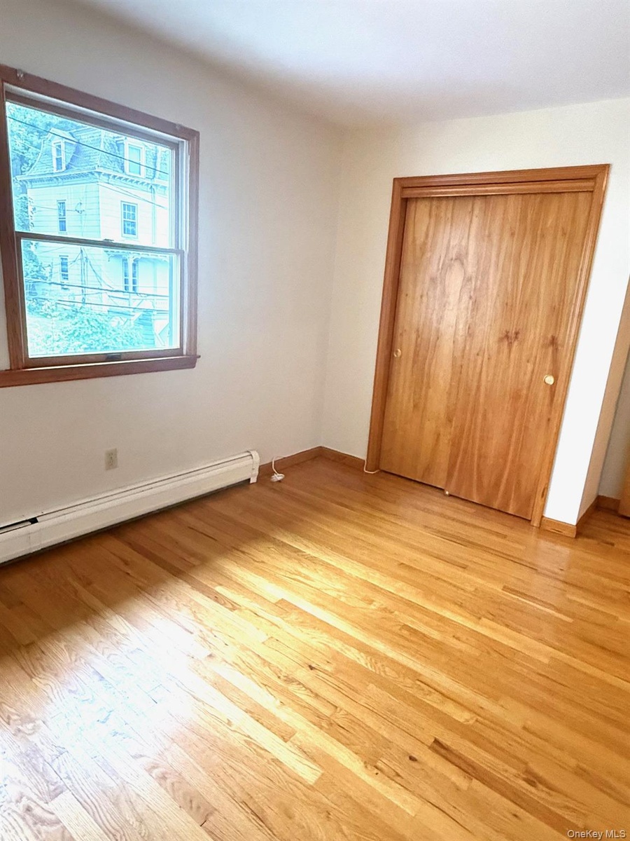 Unfurnished bedroom featuring a baseboard radiator, light wood-type flooring, and a closet